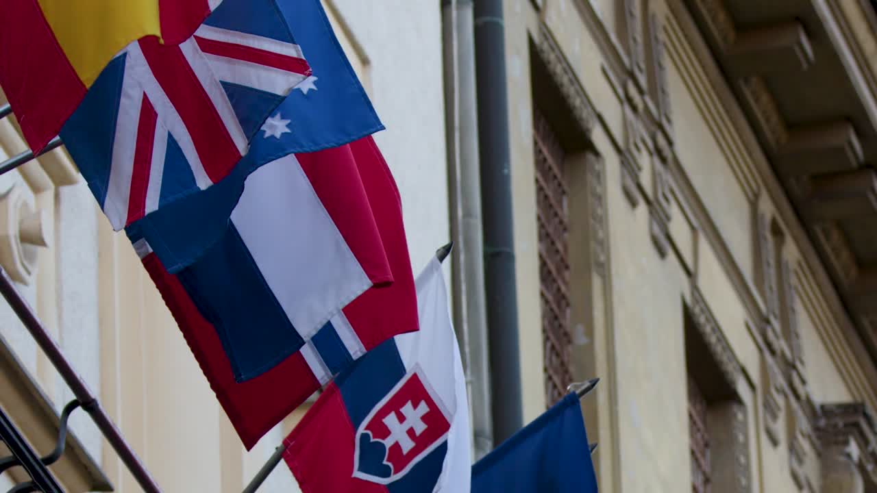 Close-up of international flags fluttering against a detailed historic embassy building in daylight