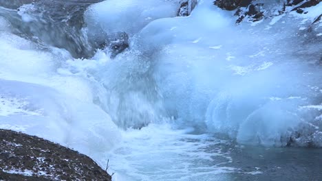 un río en movimiento rápido que fluye sobre rocas cubiertas de hielo a principios de la primavera