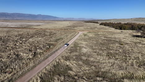 Drone-shot-of-car-driving-on-dirt-road-in-Willcox,-Arizona,-wide-rising-aerial-shot