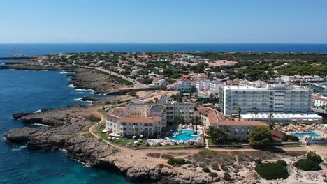 Aerial-shot-of-people-on-vacation-on-beautiful-beach-cove-near-holiday-complex-in-Menorca,-Spain