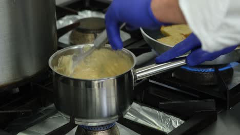 cocina profesional cerca de las manos del chef usando guantes revolviendo salsa de crema de champiñones en una olla de acero inoxidable, preparación de comida sabrosa