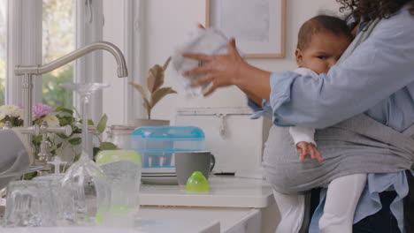 happy mother holding baby working at home washing dishes cleaning kitchen caring for toddler doing housework enjoying motherhood