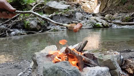 guy takes well done sausages from camp fire to eat next to river