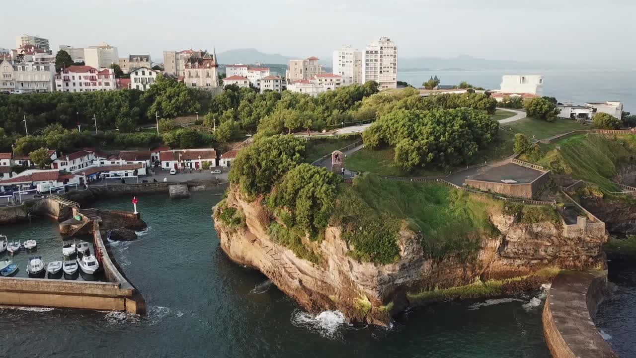 Port des Pêcheurs in Biarritz, harbor, boats, rocky cliffs, and city skyline during sunset, France. Aerial drone