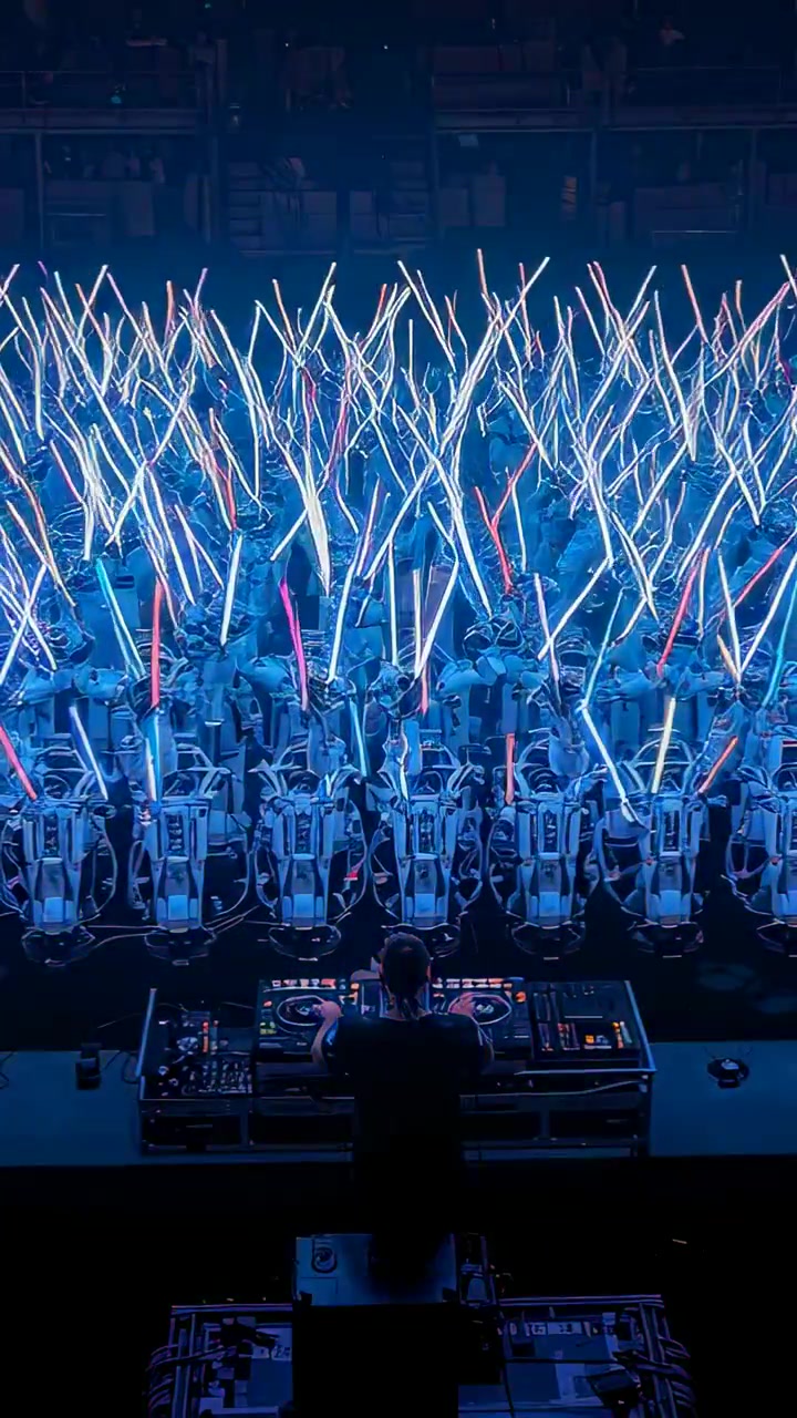 Vertical video: Directing DJ operating decks cueing mixes onstage, robots waving LED sticks