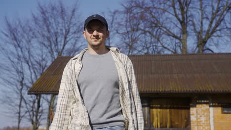 Front-view-of-a-caucasian-man-in-plaid-shirt-and-cap-holding-an-ax-and-walking-outside-a-country-house