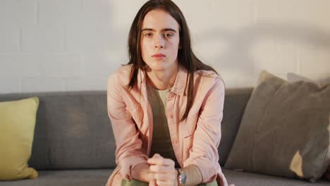 retrato de una mujer transgénero caucásica no binaria sentada en un sofá, sonriendo