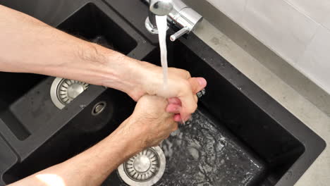 man washing hands in kitchen sink