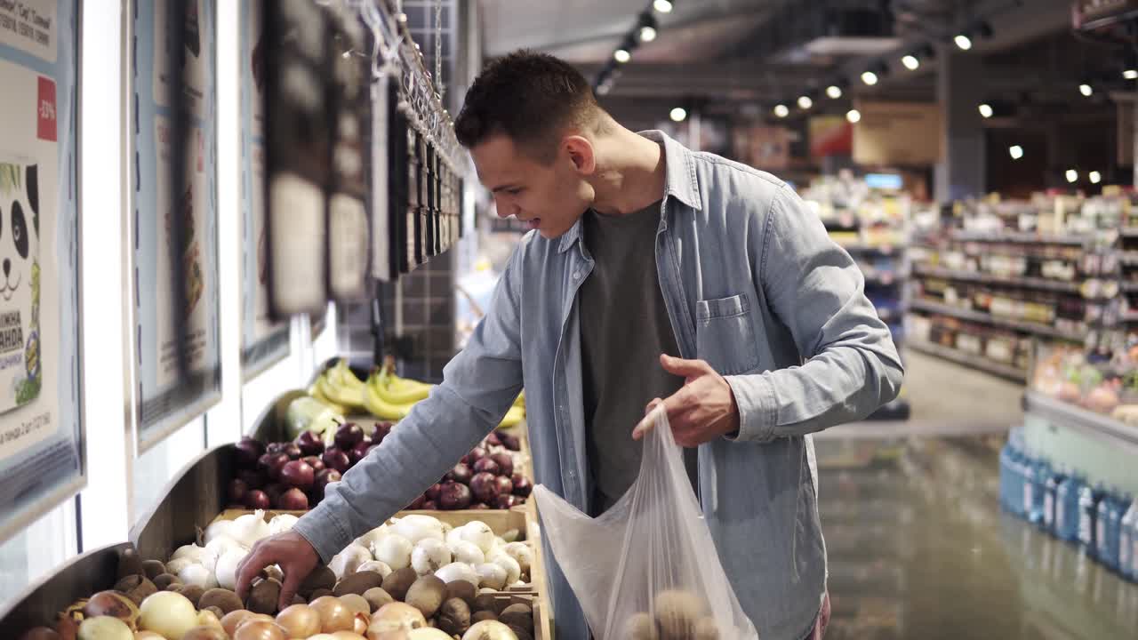 hombre caucásico guapo pone patatas en la bolsa de embalaje de plástico transparente. compras - hombre elige buenas patatas añade al paquete. gran tienda de comestibles brillante