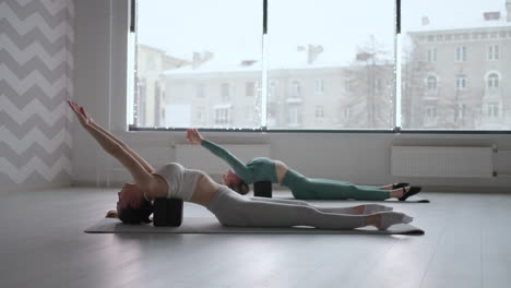 two slender young women perform back exercises lying on cubed platforms. stretching and tone of the back muscles. improvement of posture