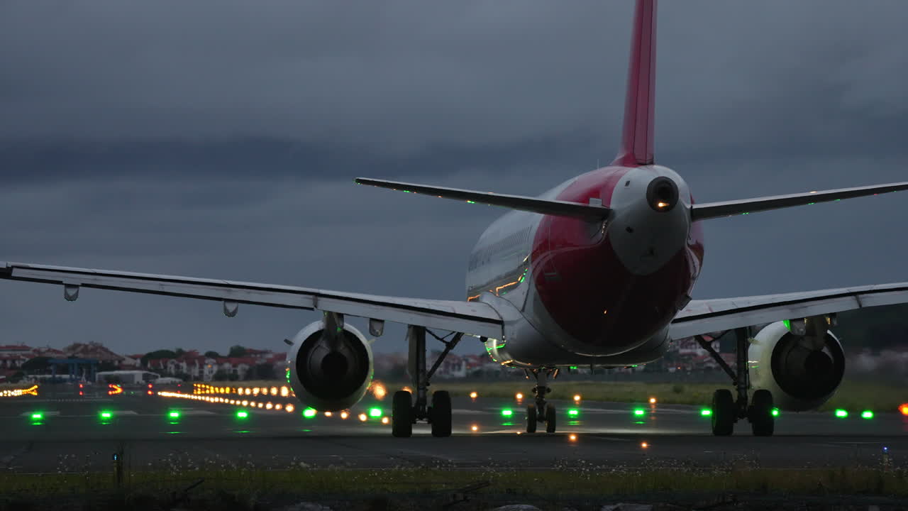Airplane positioned on runway at night, surrounded by illuminated lights and a dramatic cloudy sky, showcasing aviation and travel atmosphere