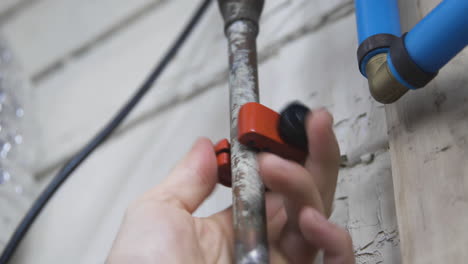 Hands-turn-a-pipecutter-around-a-copper-pipe-during-a-burst-water-pipe-repair