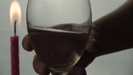 hand holding glass of white wine silhouette with candle in background close up shot