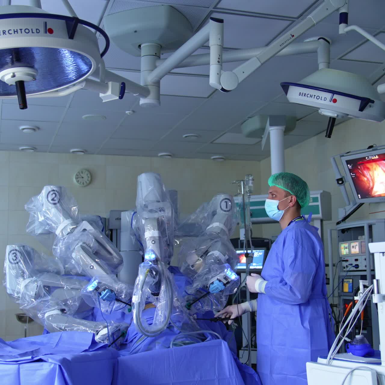 Professional surgeon cooperating with technological robot surgeon in modern surgery room. Doctor stands near the operating Da Vinci system holding a tool and looking at the screen
