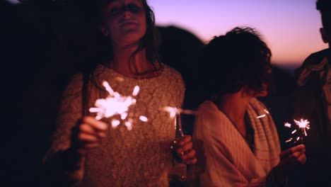 4k video footage of a young group of friends standing together on the beach and playing with sparklers at night