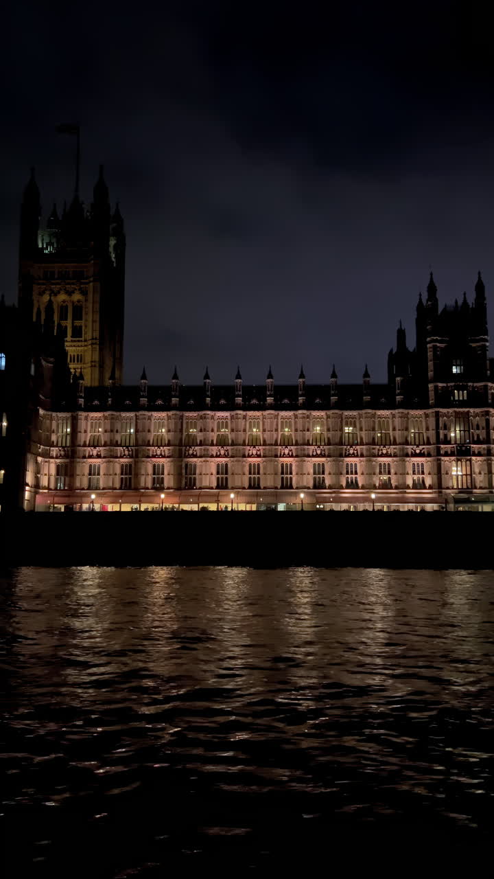 View from a moving boat of the Palace of Westminster alongside the Thames River in the evening in London, England. Vertical