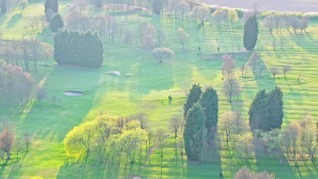 Beautiful aerial drone footage capturing a vibrant green golf course with lush fairways, scattered trees, bunkers, and soft shadows under gentle sunlight in Wombwell, South Yorkshire