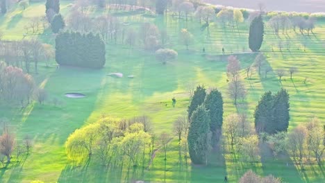 beautiful aerial drone footage capturing a vibrant green golf course with lush fairways, scattered trees, bunkers, and soft shadows under gentle sunlight in wombwell, south yorkshire