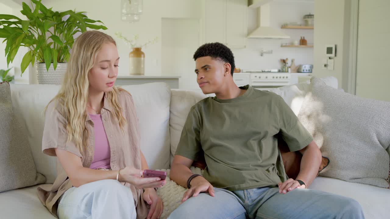 Couple sitting on couch, woman showing purple phone explaining content while man tapping screen