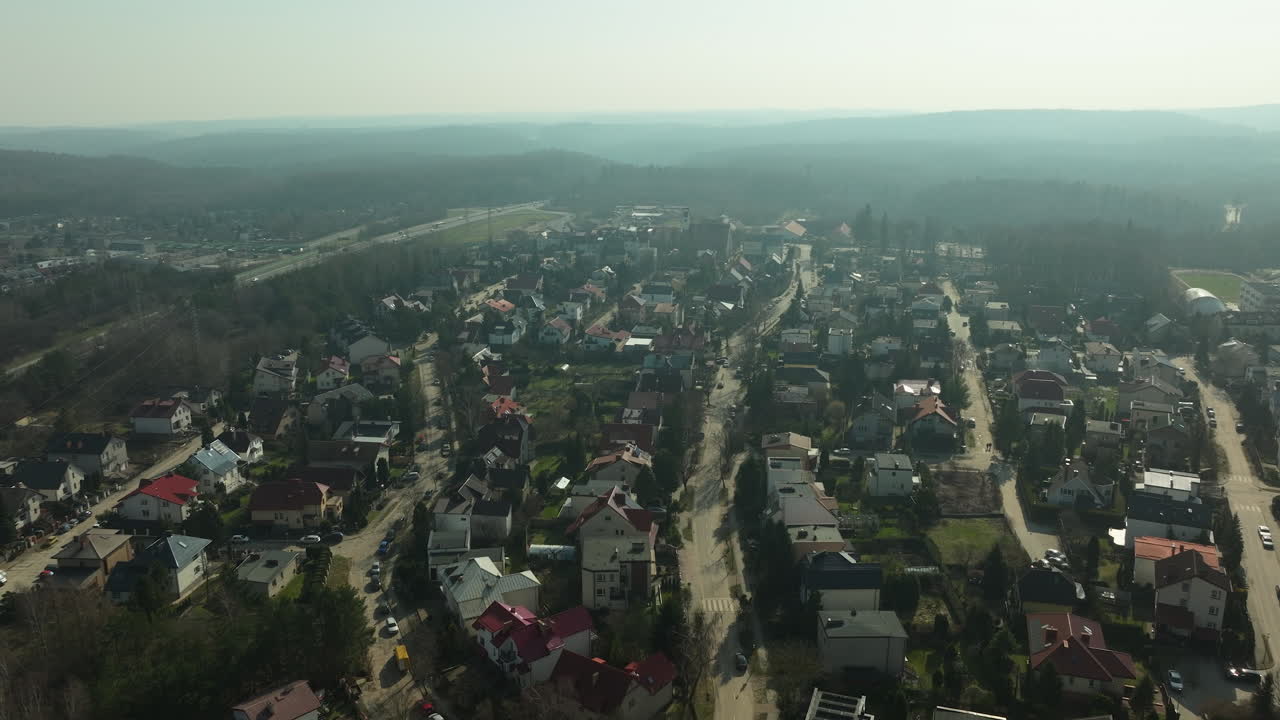 aerial view stretches over a residential street in a suburban area of Gdynia, showcasing neat homes with gardens, intersected by roads and surrounded by the bare branches of trees in winter