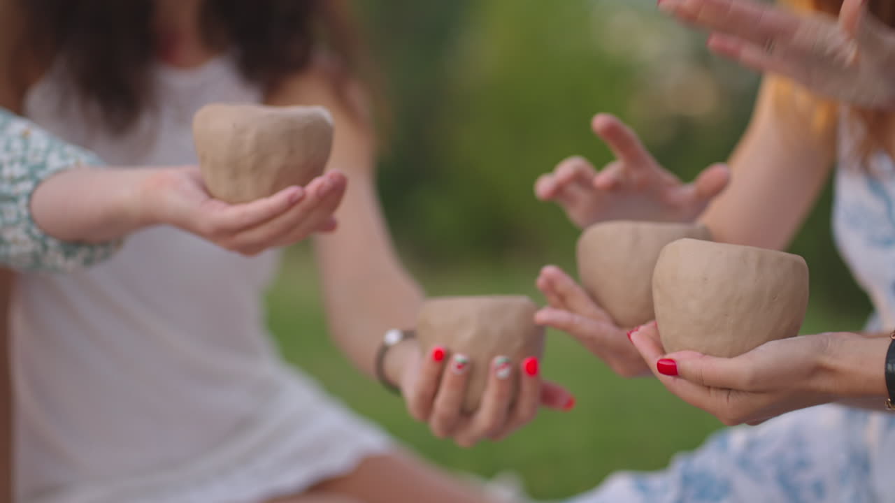 Young girls are engaged in clay modeling in nature in the park in the open space. Group creative classes training in clay modeling. Women's hands hold clay products in close-up.