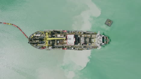 Wide-top-down-aerial-footage-of-a-ship-that-is-dredging-up-sand-in-the-harbor-of-Bari,-Italy-during-the-bright-day