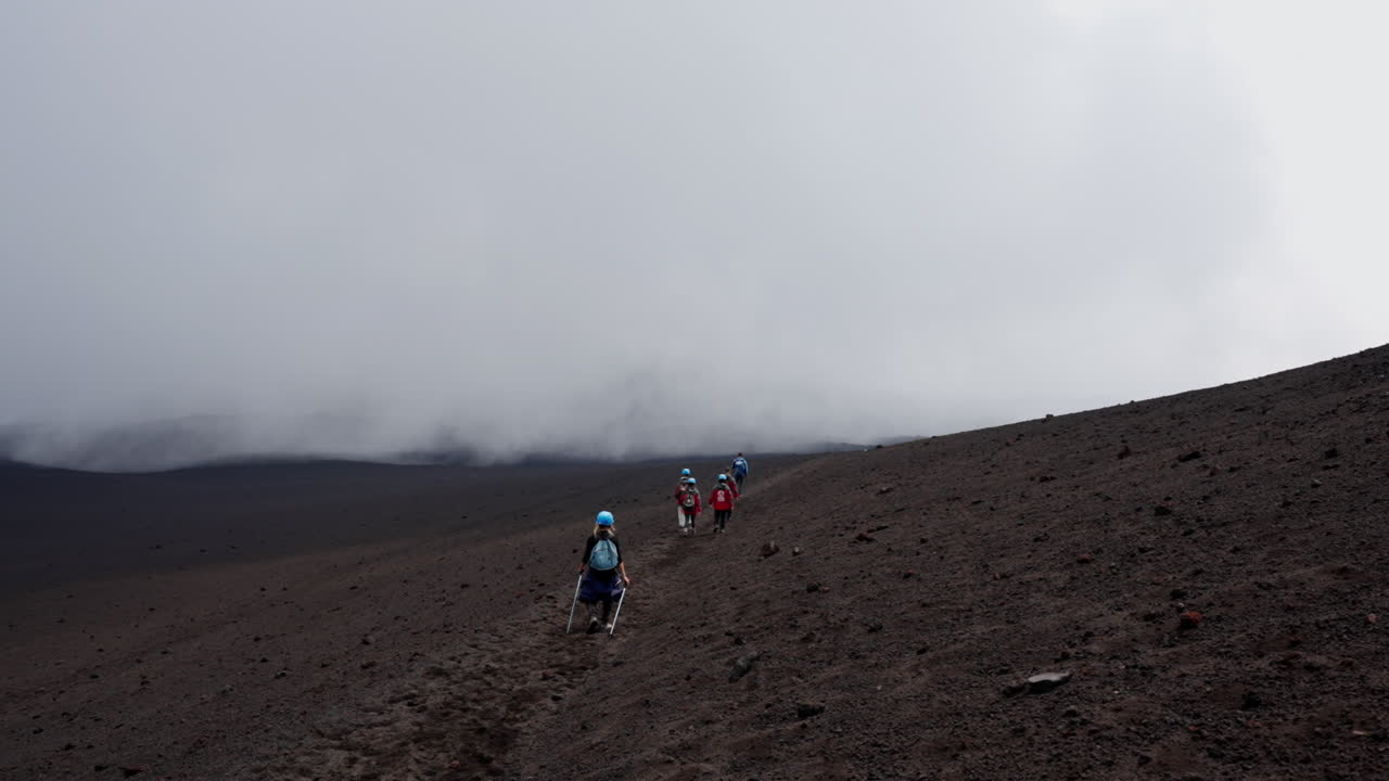 Hikers on Mount Etna's rugged slope under cloudy skies in Sicily