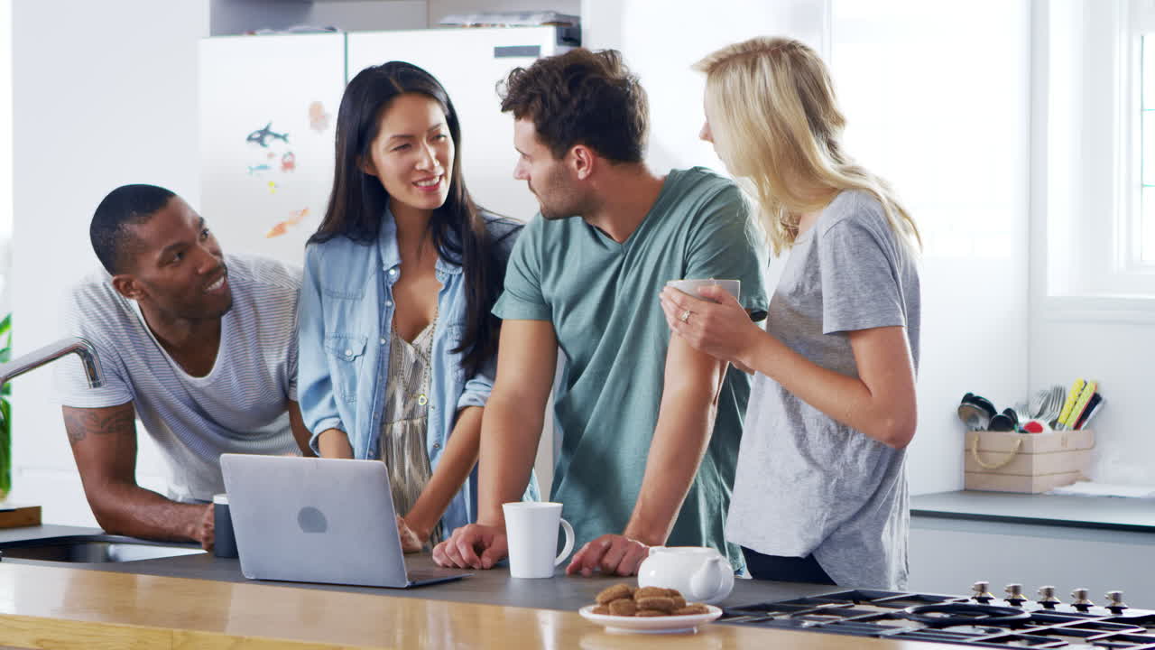 Friends Looking At Laptop And Drinking Coffee In Modern Kitchen