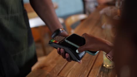 persona afroamericana pagando con un teléfono inteligente en una cafetería