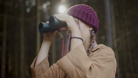 female explorer observing through binoculars in forest