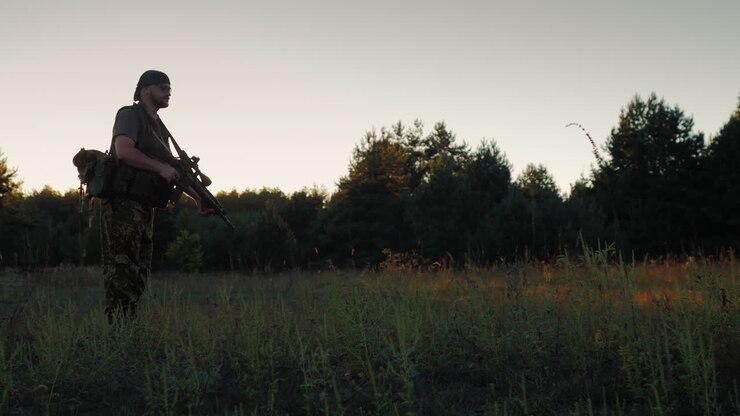 Un uomo armato in corsa all'attacco, con l'arma in mano, al tramonto.