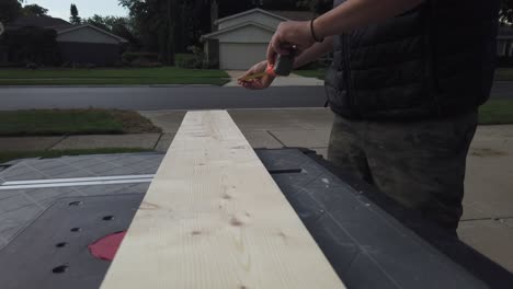 white male measuring wood board with a tape measure in the day