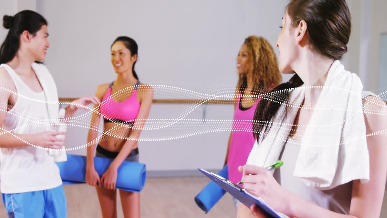 Fitness instruktor si zapisuje na schránku s klipem, zatímco účastníci vstupují do jógového studia s podložkami na lekci.