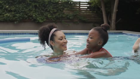 Happy-diverse-mother-with-daughter-swimming-in-pool-in-garden-in-slow-motion