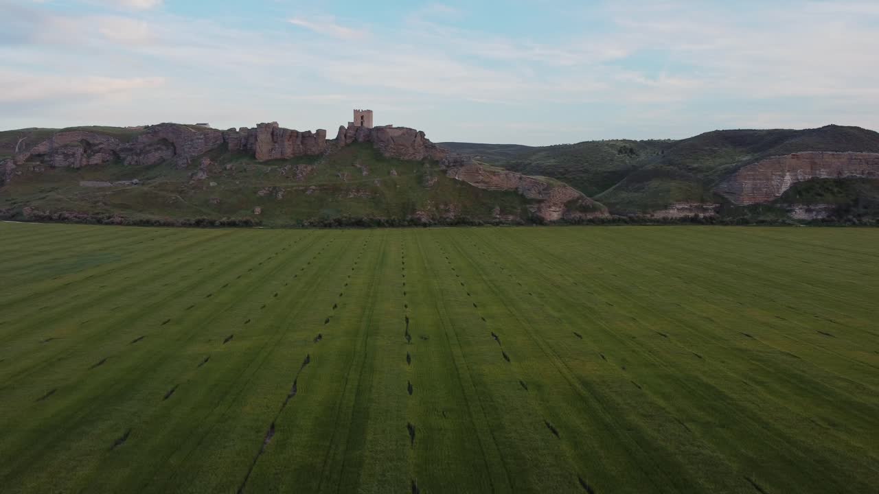 Aerial view of lush green crop fields with an ancient hilltop castle in the background near Aranjuez, Spain. Scenic rural landscape with medieval architecture.