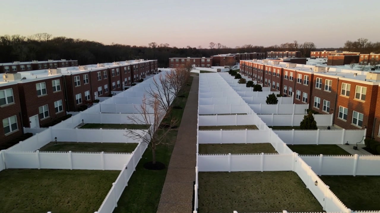 Launching drone gliding along central paved path at complex, revealing white fences, leafless trees