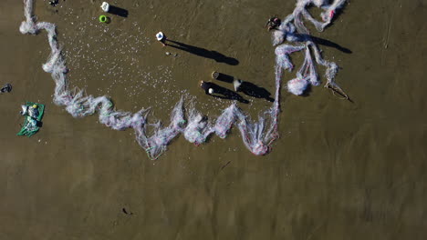 aerial top down, fishermen sort out big catch of fish from fishing net on beach