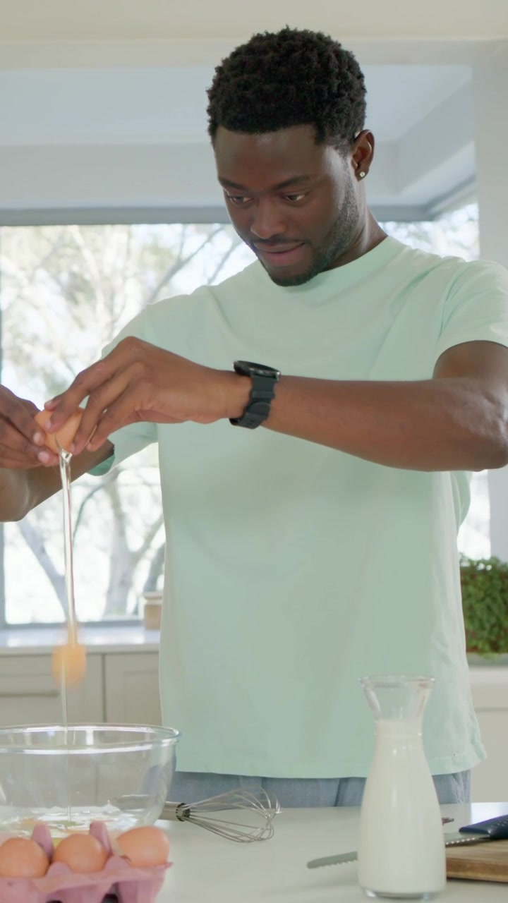 Vertical video: Picking egg, man in mint tee cracking eggs into bowl in kitchen for breakfast