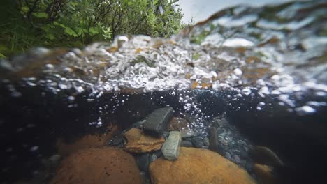 An-over-under-water-view-of-the-shallow-river-with-rocky-bottom-and-banks-covered-with-greenery