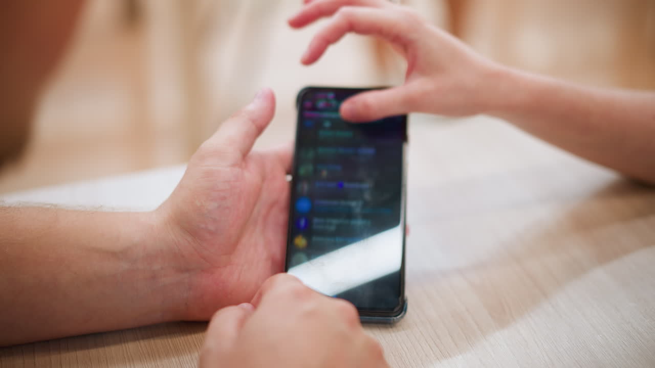 primer plano de manos sosteniendo el teléfono inteligente con una mano operando el dispositivo, usando un anillo, la pantalla muestra una interfaz de aplicación de mensajería, la iluminación se refleja suavemente en el teléfono