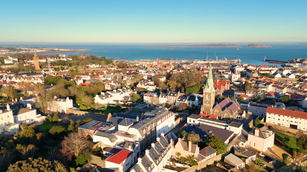 High panning drone footage of the roof tops of St Peter Port Guernsey in the golden hour with views across town and the harbour to Herm and Jethou