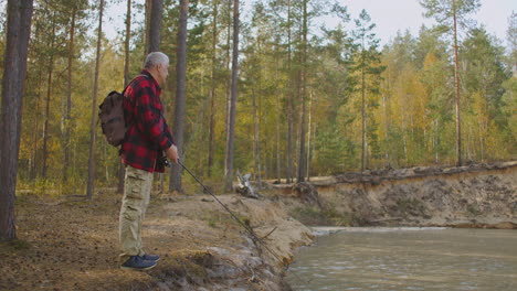 Erwachsener-Mann-Angelt-Fische-Im-See-Im-Wald-Mit-Spinnrute,-Steht-An-Der-Küste-Im-Wald.-Wanderer-Fischt