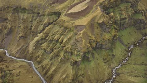 aerial shot of a winding river flowing through a steep, moss-covered canyon in brókarjökull, iceland, highlighting the rugged landscape and earthy textures