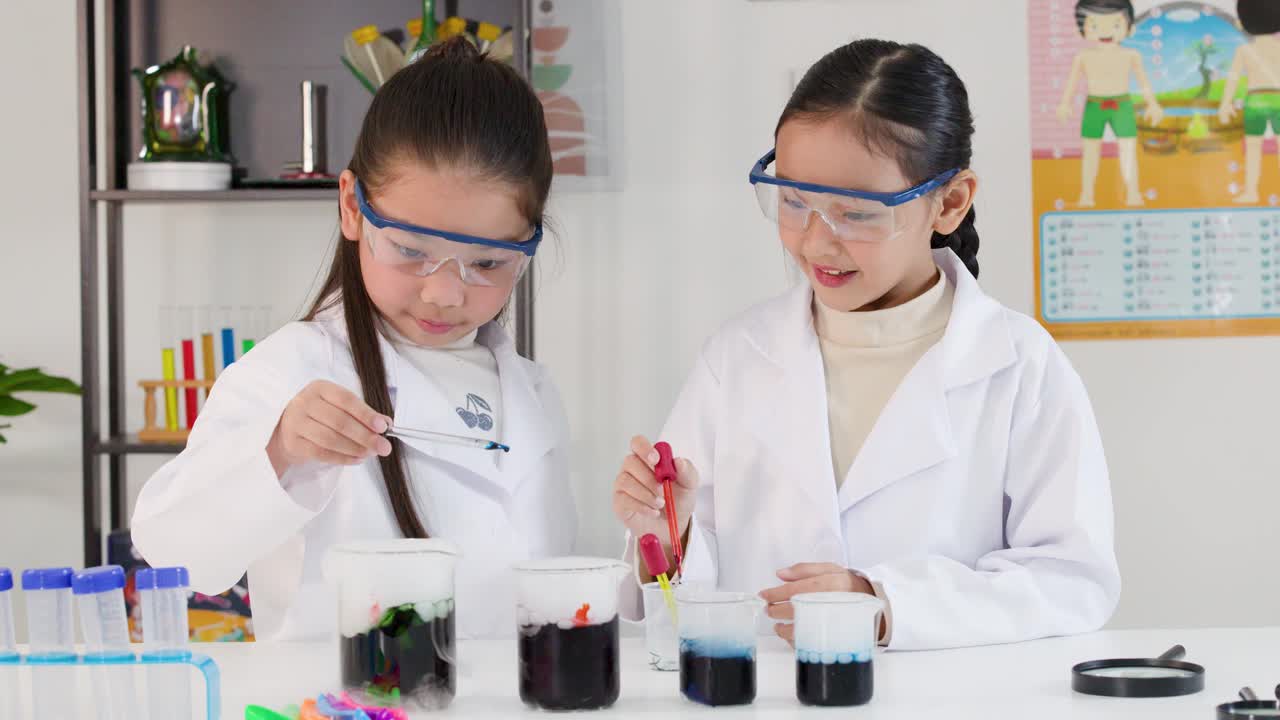 Siswi-siswi Asia mengenakan kacamata pengaman menggunakan pipet tetes dan gelas kimia untuk percobaan kimia di ruang kelas.