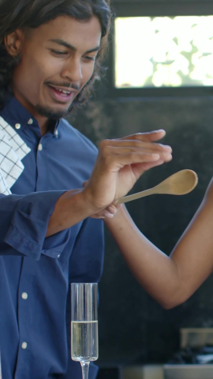Video verticale: Donna in abito color crema che spreme la salsa e la spalma su una base per pizza al bancone, mentre un uomo aggiunge ingredienti.