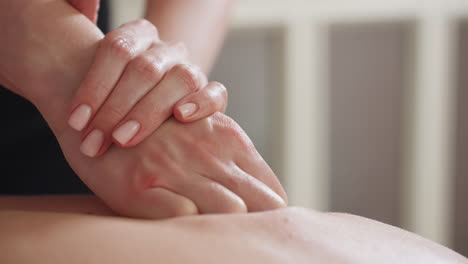 closeup of light skin woman with well-groomed nails performing massage on client back using gentle pressure, showcasing relaxation technique in calm indoor environment with soft natural lighting