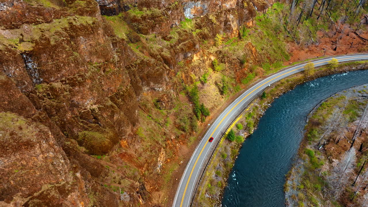 Descend approaching red car riding by the highway at the foot of the bare rock. Beautiful narrow sea-green river flowing nearby.