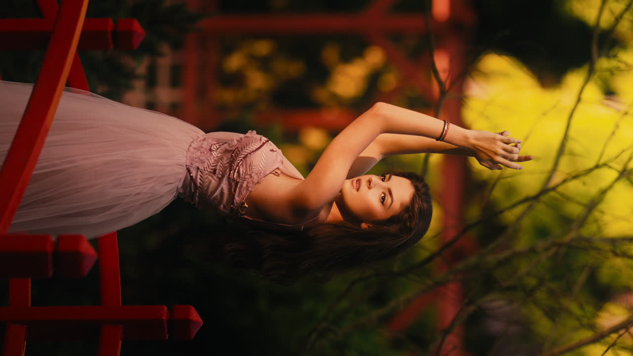 젊은 백인 여성 모델은 긴 분홍색 드레스를 입고 정원 수직 비디오에서 팔로 놀고 있습니다.