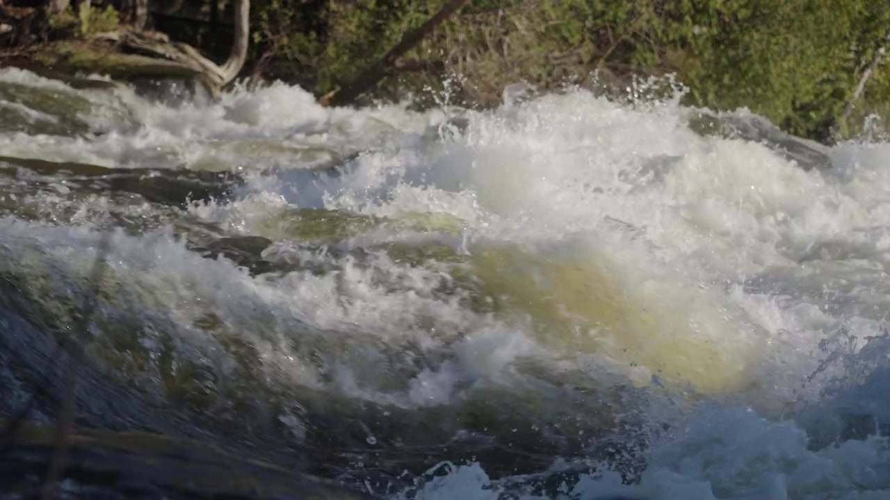 Forti correnti attraversano un letto di fiume roccioso durante l'alta portata primaverile sulla penisola di Bruce. L'angolazione ravvicinata della fotocamera cattura la schiuma caotica e il rapido movimento delle cascate di Sauble in Ontario.