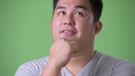 young handsome overweight asian man against green background